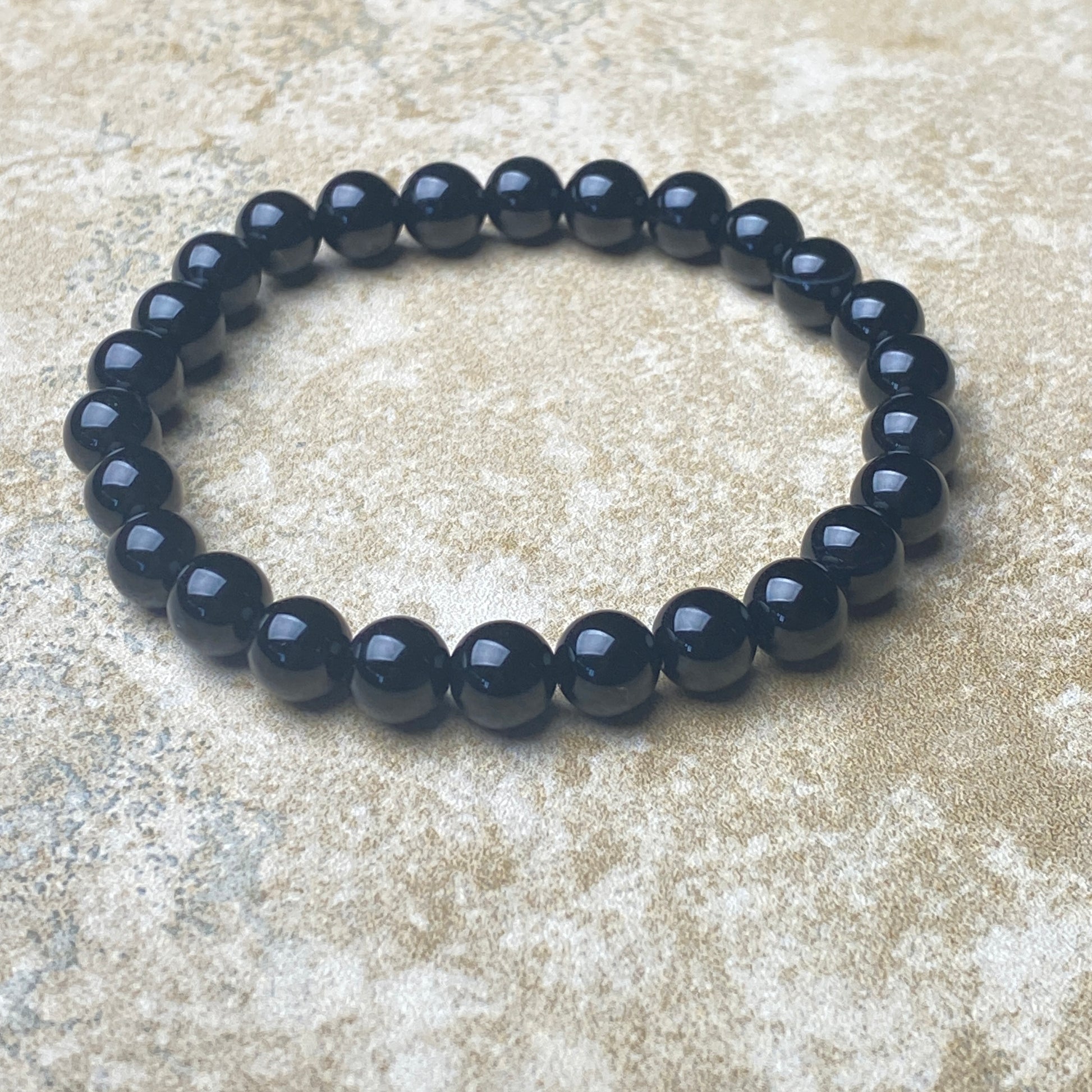 Black beaded bracelet on a textured beige surface