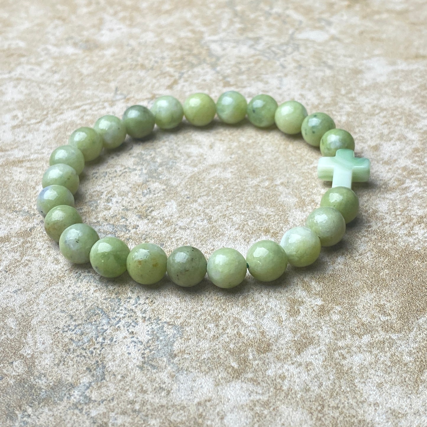 Green beaded bracelet with a cross charm on a textured beige surface