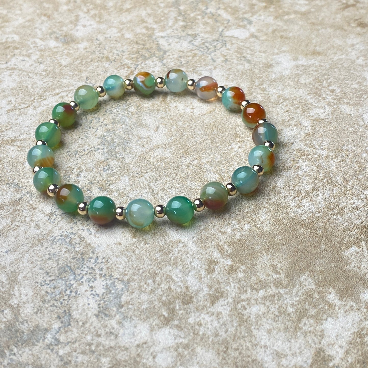 Beaded bracelet with green and brown beads on a textured surface