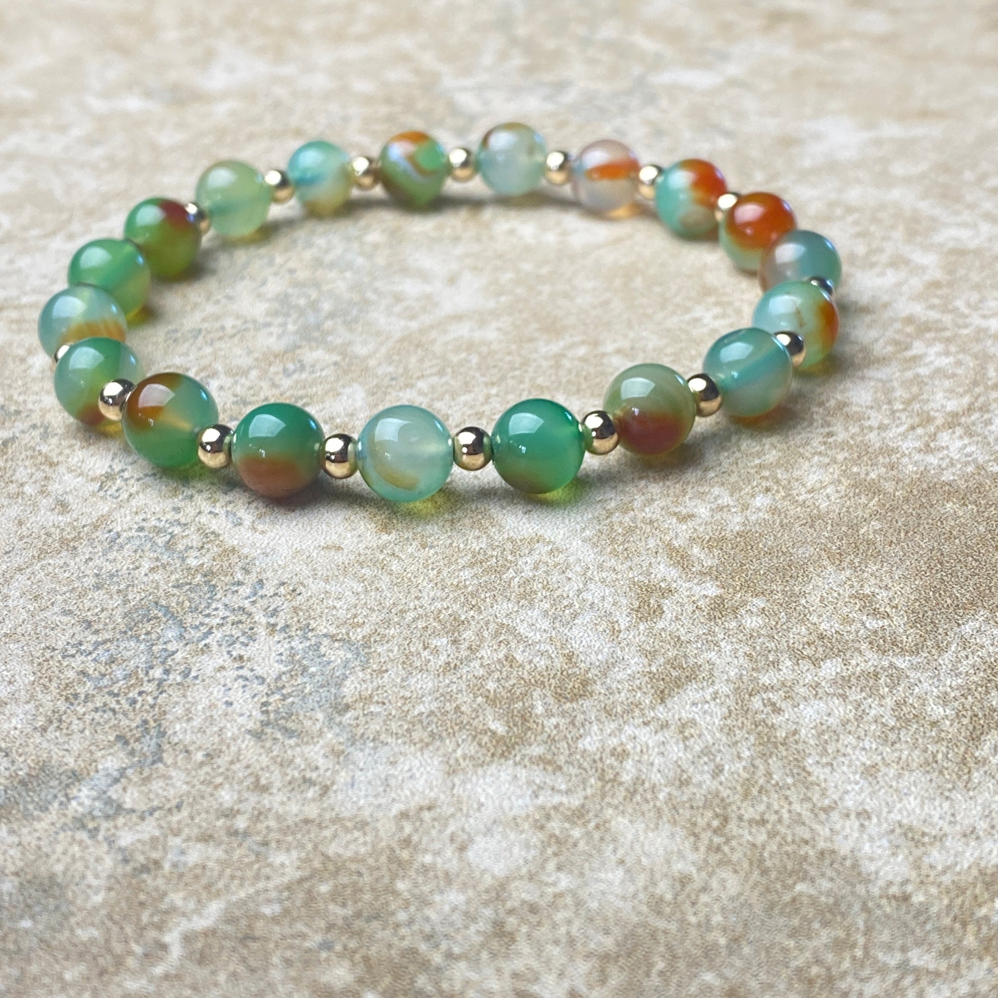 Beaded bracelet with green and gold beads on a textured surface