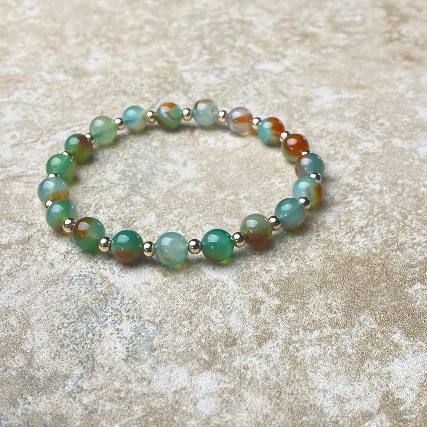 Beaded bracelet with green and brown beads on a textured beige surface
