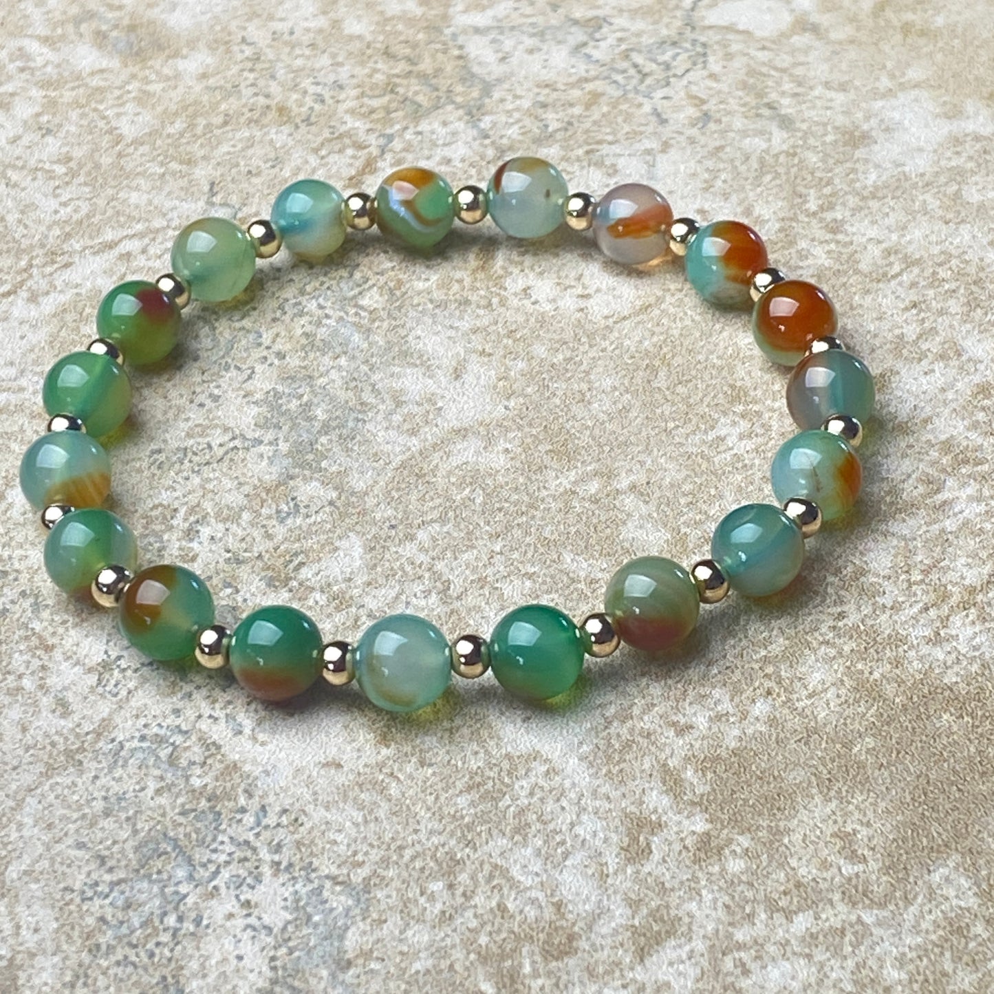Beaded bracelet with green and brown beads on a textured surface