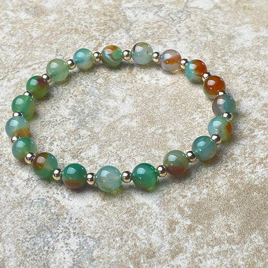 Beaded bracelet with green and brown beads on a textured surface