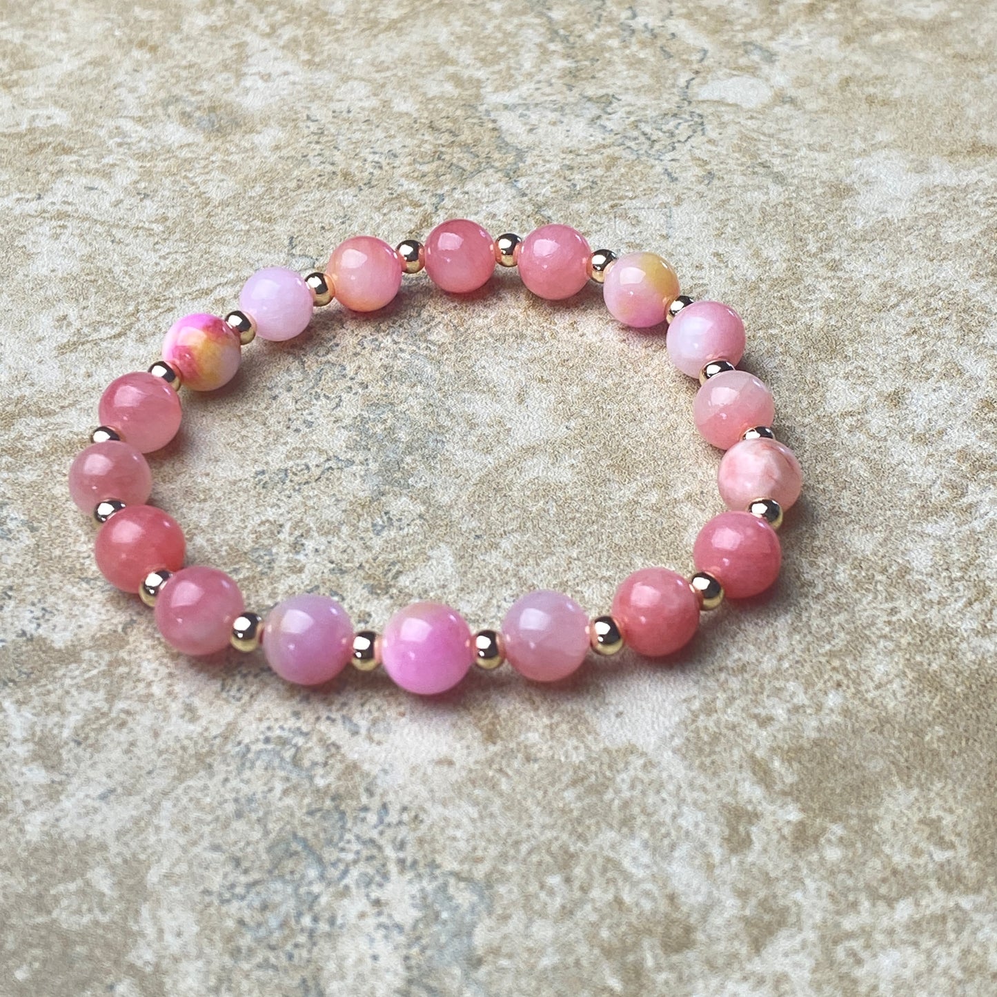 Pink beaded bracelet on a textured beige surface