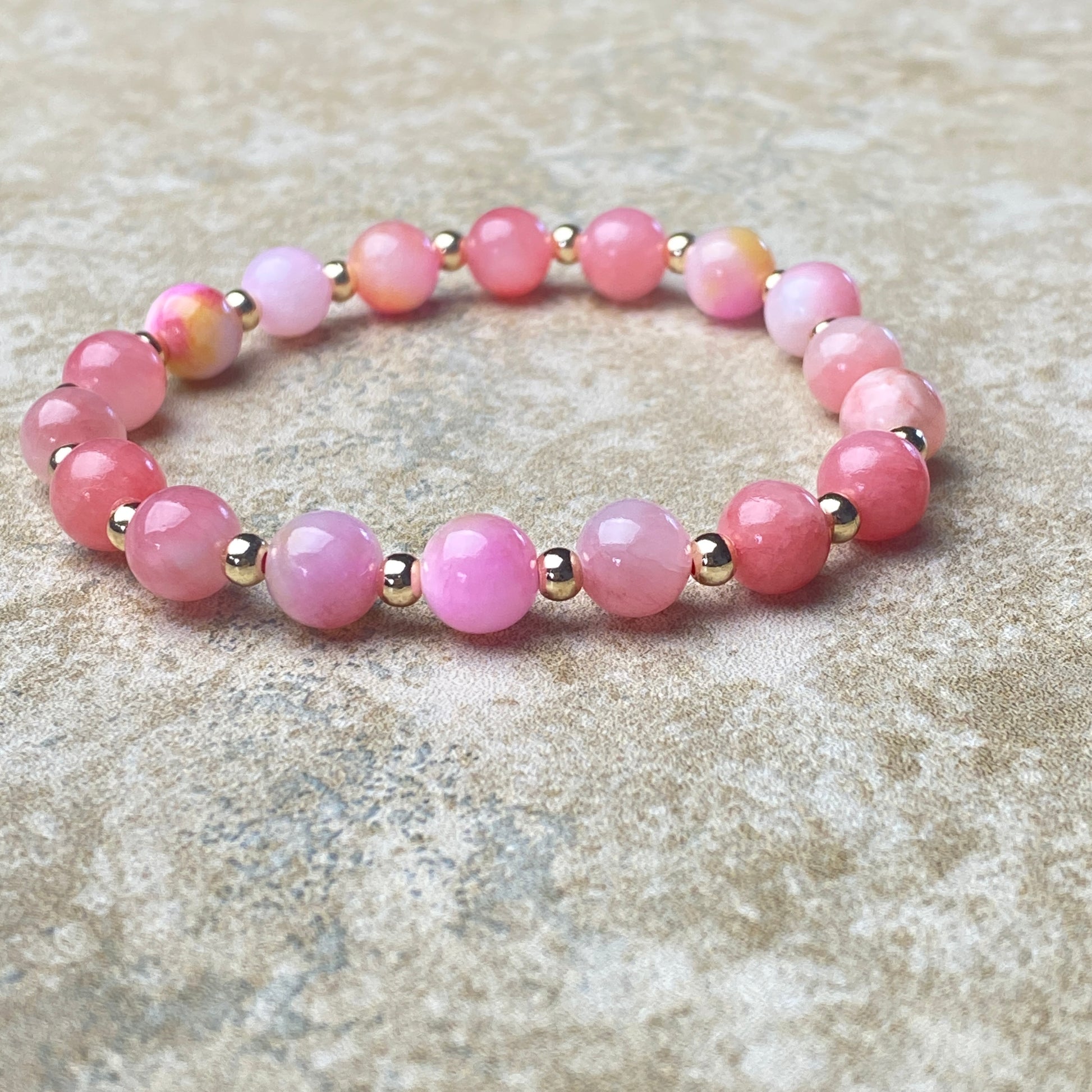 Pink beaded bracelet with gold accents on a textured surface