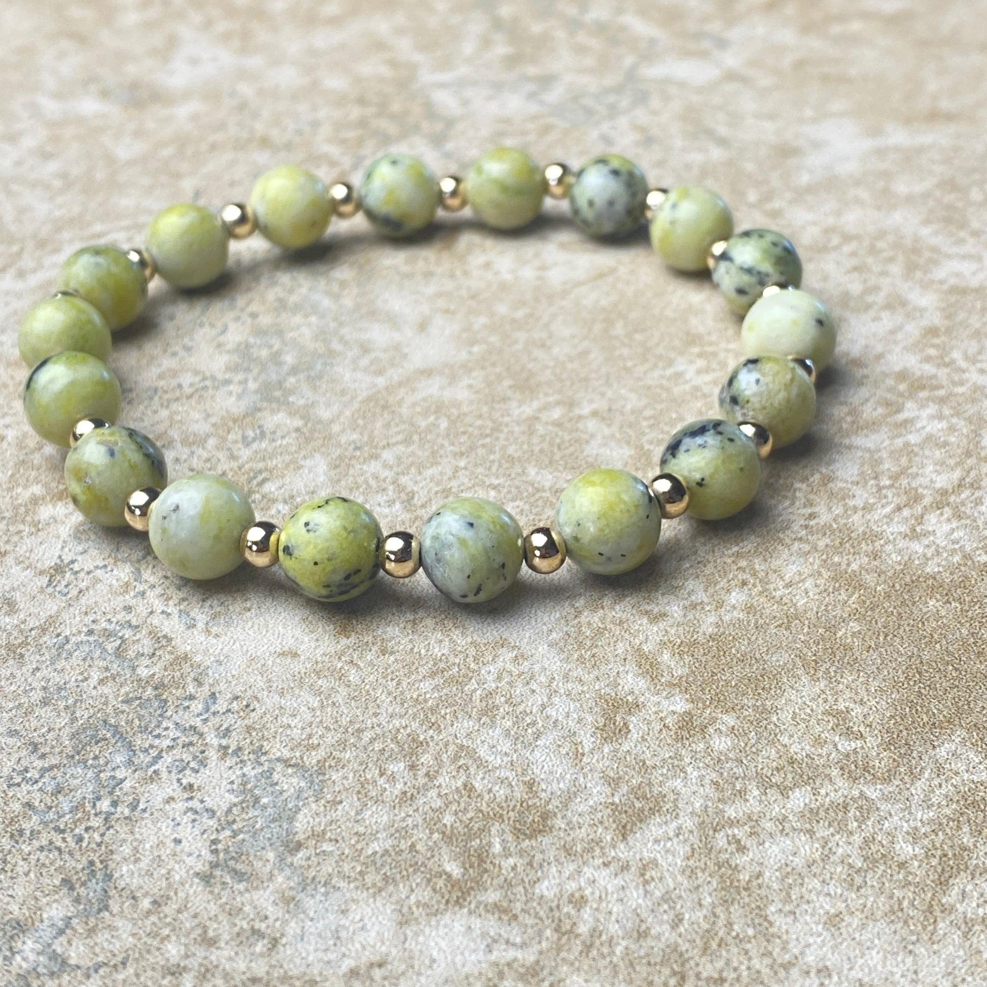 Beaded bracelet with green beads and gold accents on a textured surface