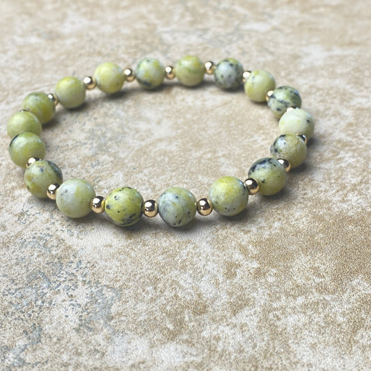 Beaded bracelet with green beads and gold accents on a textured surface
