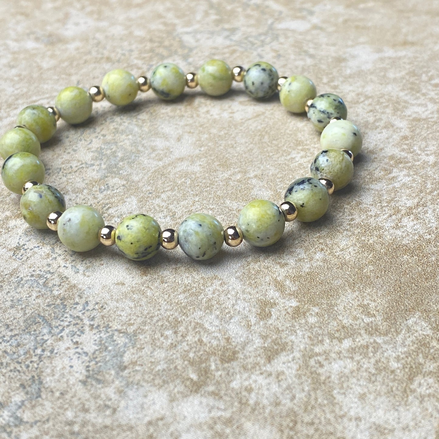 Green beaded bracelet on a textured beige surface