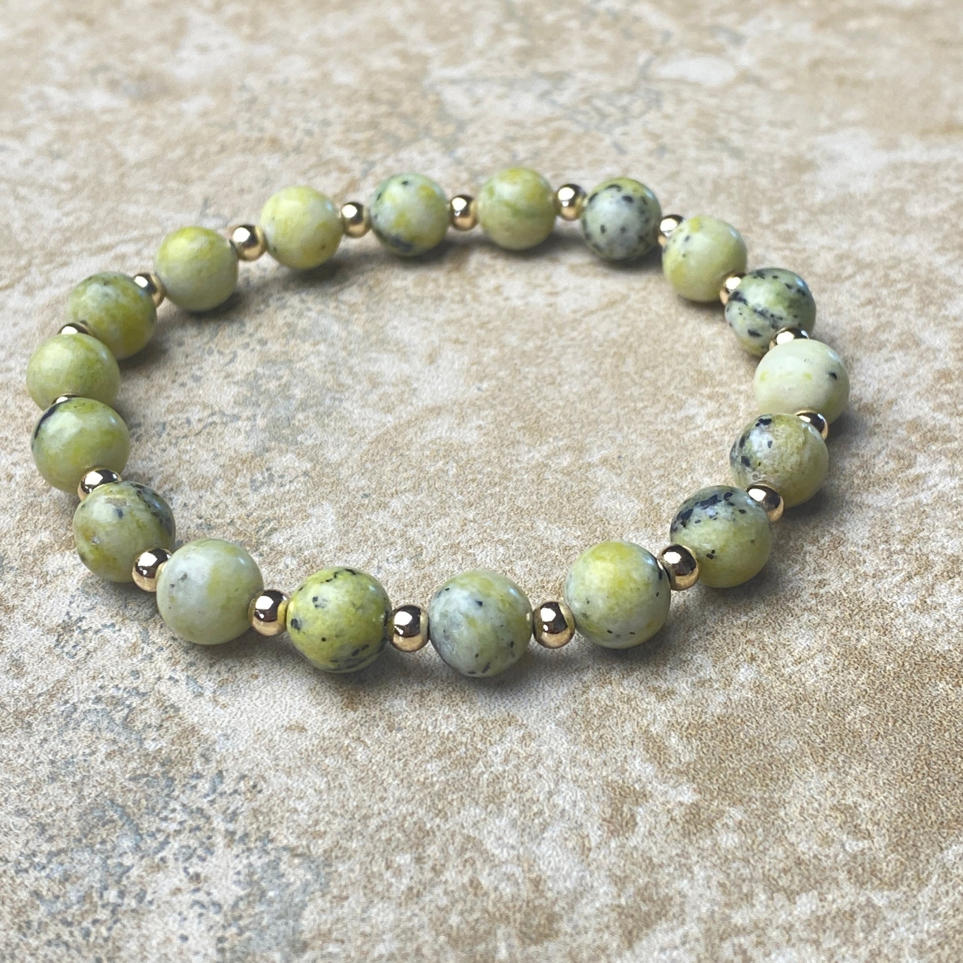 Green beaded bracelet with gold accents on a beige surface