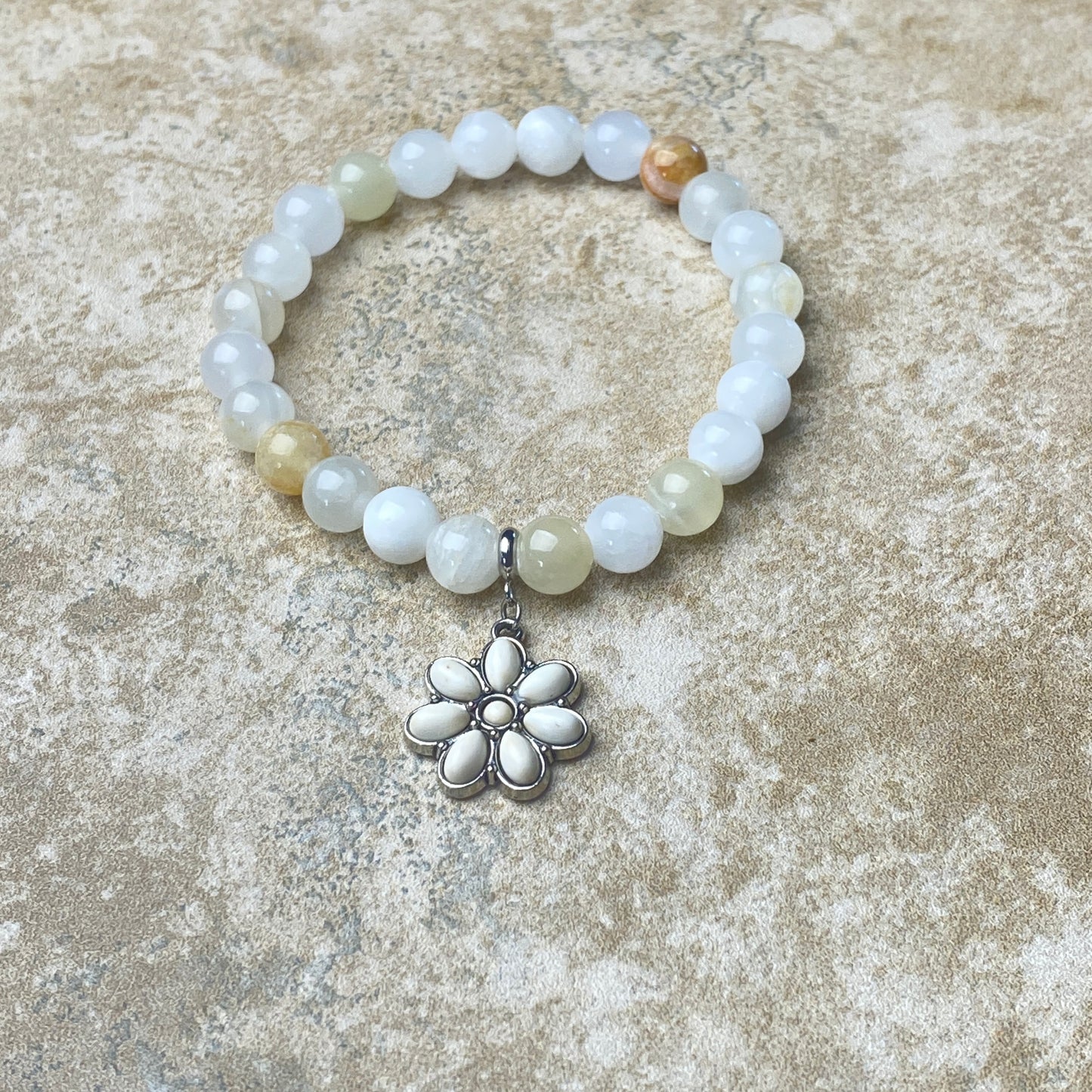 Beaded bracelet with a silver flower charm on a textured surface