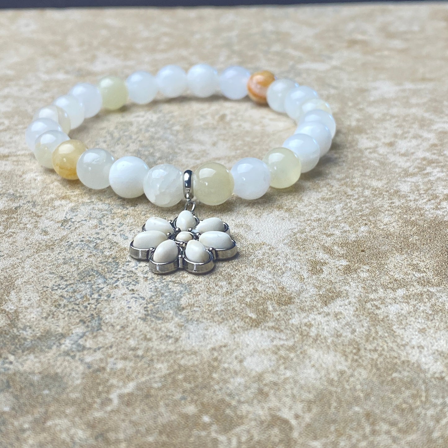 Beaded bracelet with a silver flower-shaped charm on a textured surface