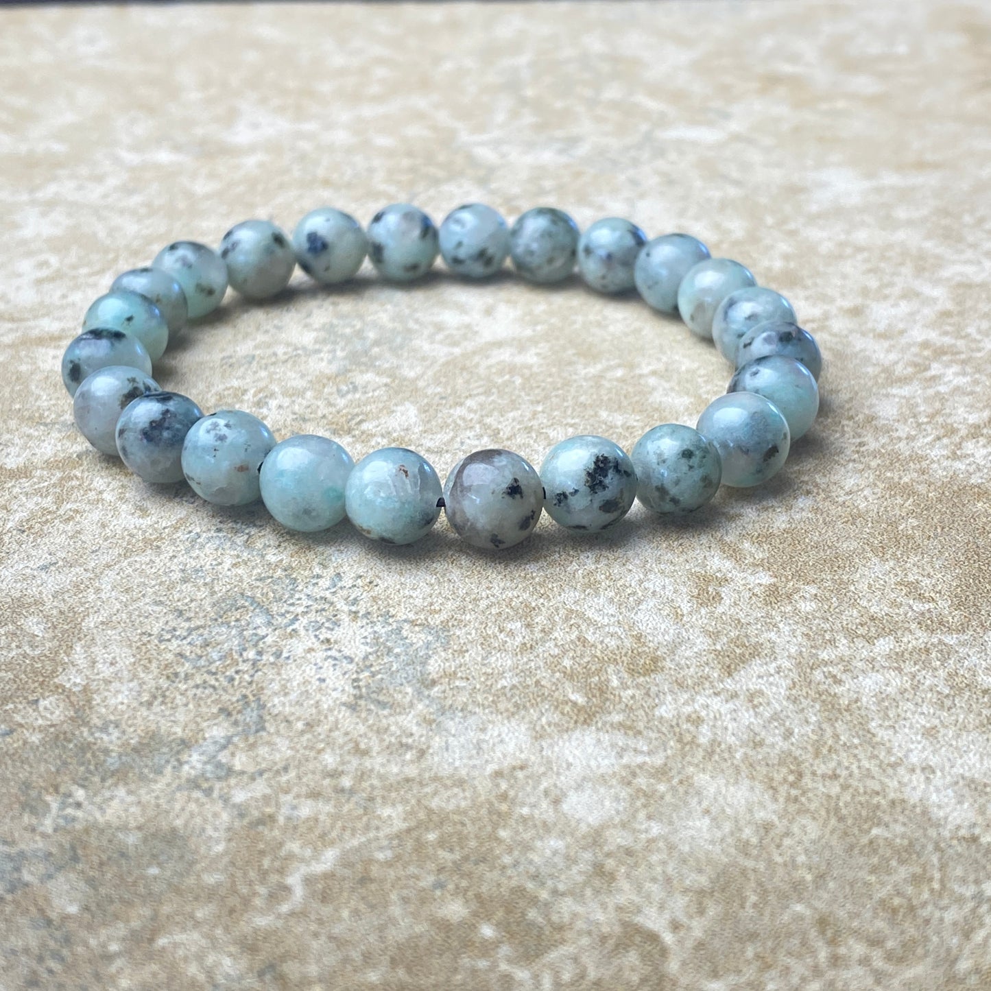Beaded bracelet with blue and gray stones on a textured beige surface