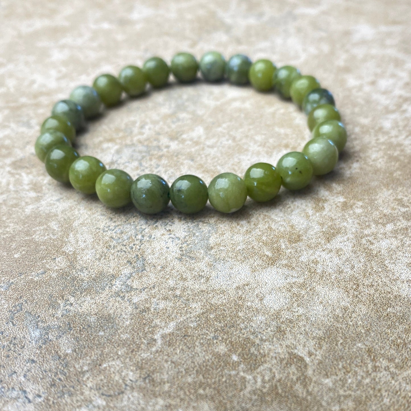 Green beaded bracelet on a textured beige surface