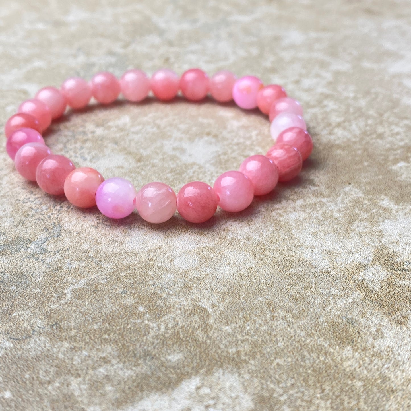 Pink beaded bracelet on a textured beige surface