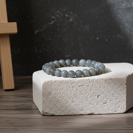 Gray beaded bracelet on a textured white block with a dark background