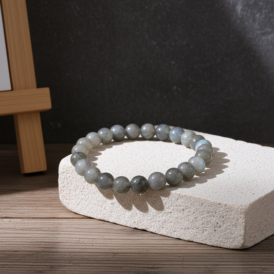 Gray beaded bracelet on a white stone surface with a dark background