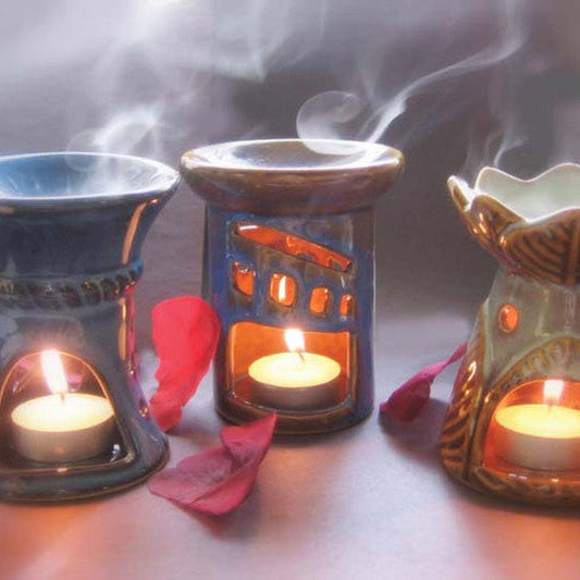 Three ceramic oil burners with candles inside, emitting smoke on a reflective surface.