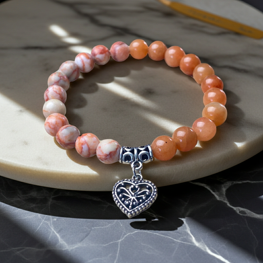 Beaded bracelet with a silver heart charm on a marble surface