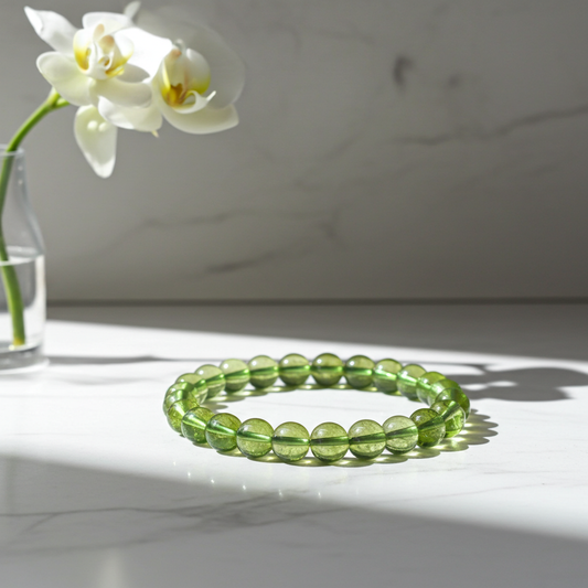 Green beaded bracelet on a white surface with a white orchid in the background
