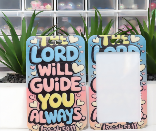 Colorful ID holder with motivational quote 'The Lord will guide you always' on a white surface with plants in the background.