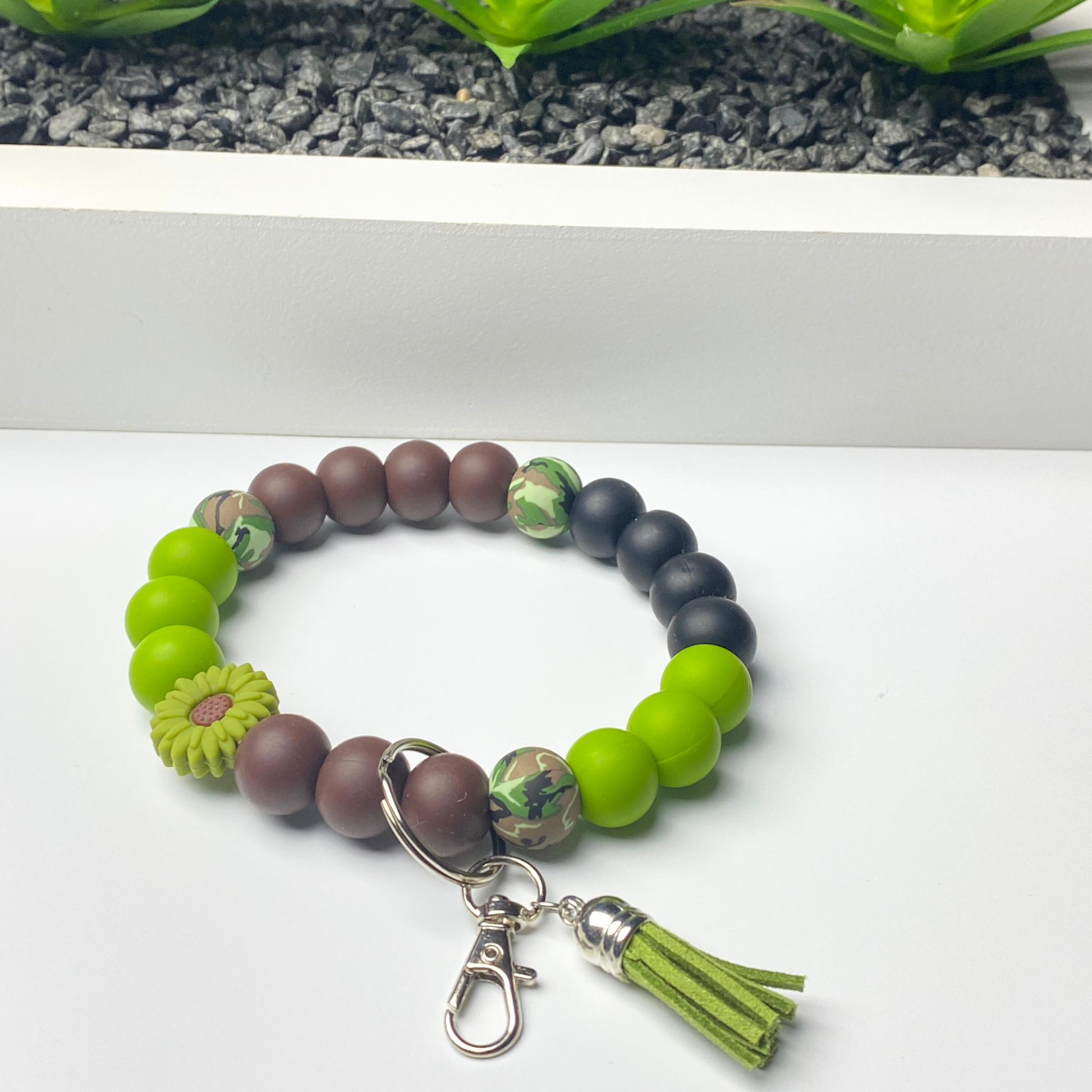 Beaded bracelet with green and brown beads and a tassel charm on a white background.