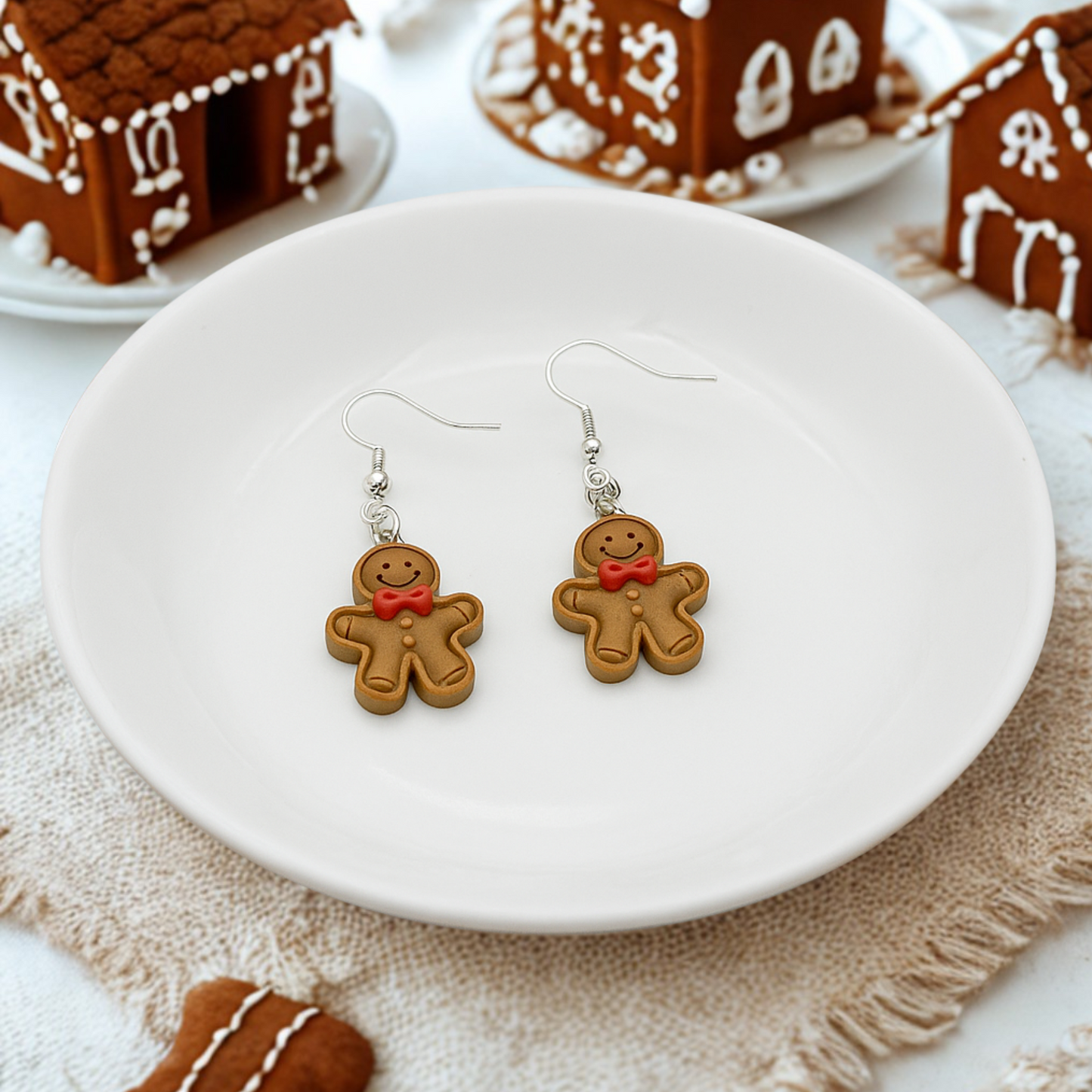 Gingerbread man earrings on a white plate with gingerbread houses in the background.