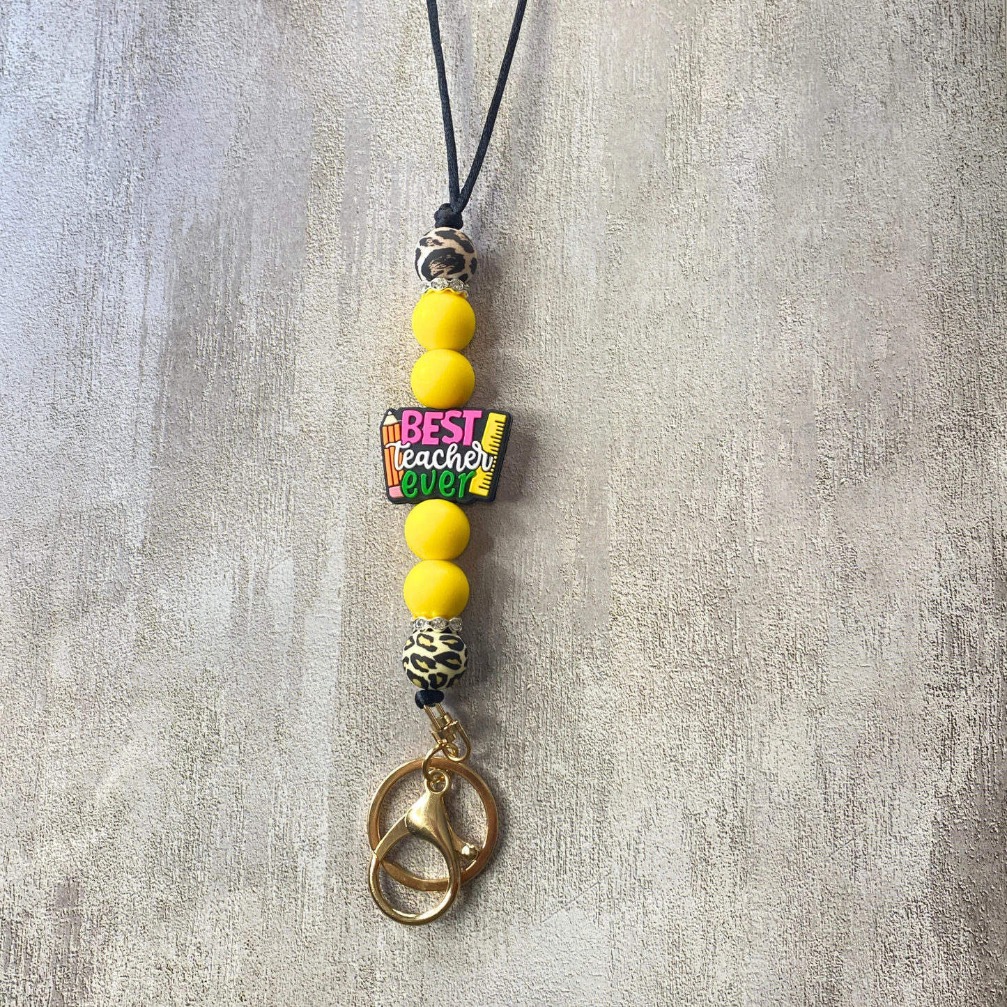 Necklace with yellow beads and a tag reading 'Best Teacher Ever' on a textured gray background