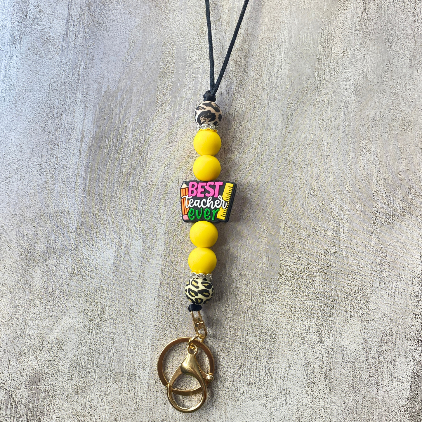 Beaded charm with 'Best Teacher Ever' text on a gray background