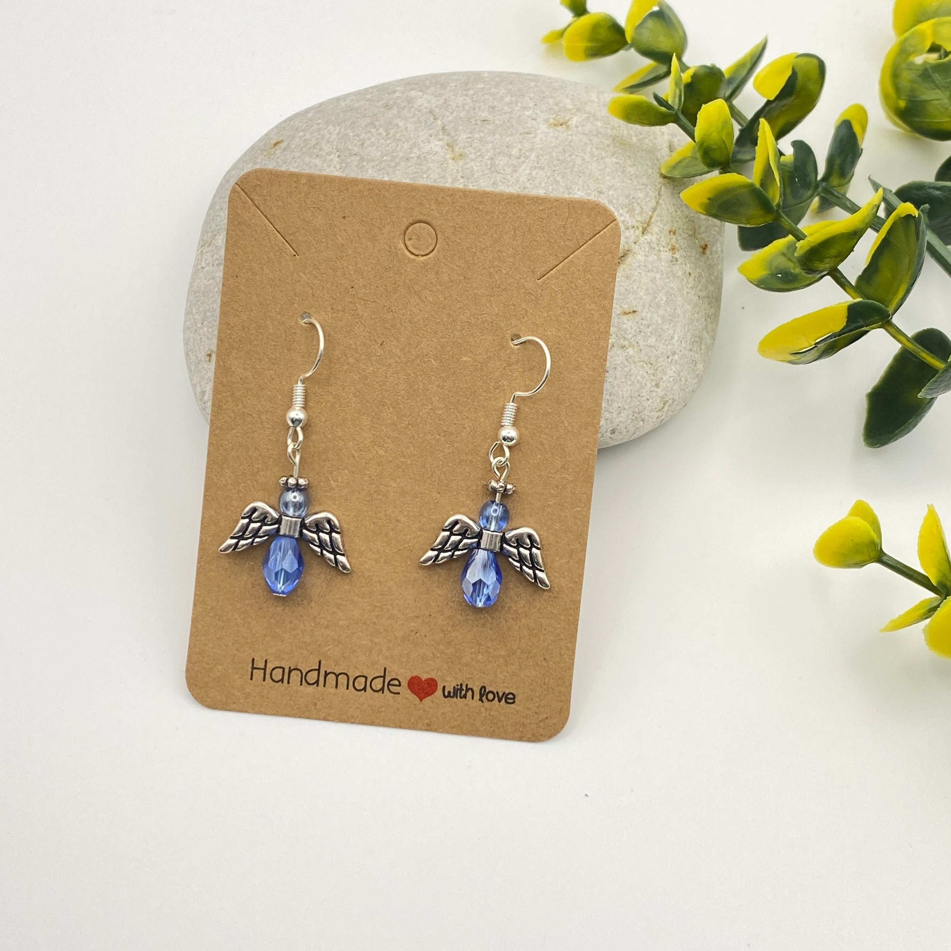 Pair of angel wing earrings on a 'Handmade with Love' card with green leaves in the background.