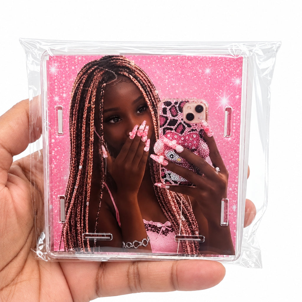 A hand holding a clear plastic-wrapped square phone case featuring a pink mirror-selfie design with a woman and a pink patterned phone.