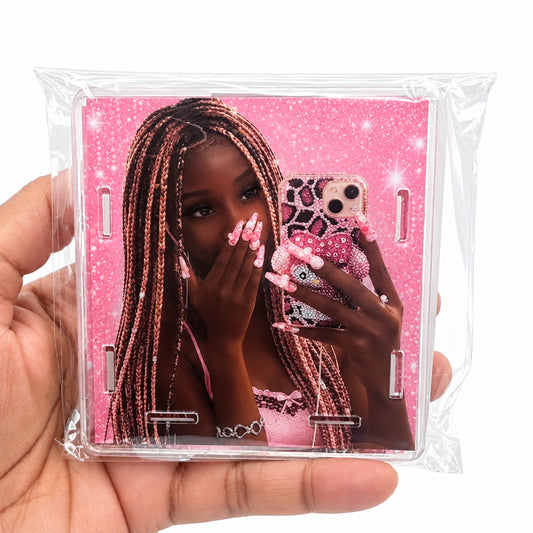A hand holding a clear plastic-wrapped square phone case featuring a pink mirror-selfie design with a woman and a pink patterned phone.